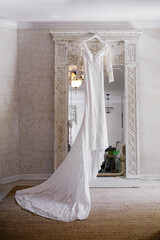 Elegant lace wedding dress hanging by ornate mirror