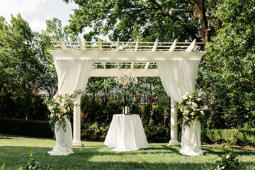 Outdoor wedding ceremony with white draped pergola and floras