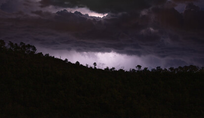 Dark clouds over a silhouette of trees at night, storm looming