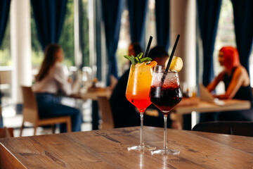 Two colorful cocktails on a restaurant table with people