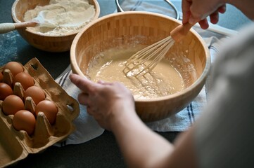 Woman preparing pancake dough at home in a wooden bowl