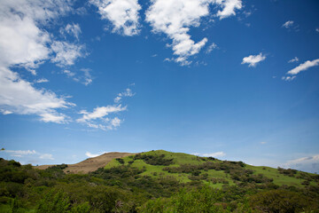 Lush green hills under a blue sky with clouds in Costa Rica.