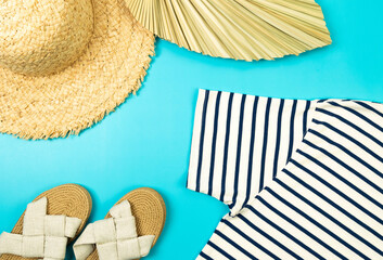 Top view of straw hat, slippers, dried palm leaf and striped t-shirt on blue background. Summer...
