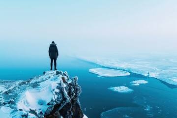 A person stands on a cliff's edge overlooking vast icy waters and floating ice floes, with a clear...