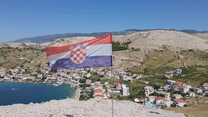 Croatian flag on a rock cliff over the Adriatic sea with a characteristic old traditional village...