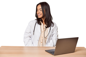 Young Filipino doctor with laptop in studio looks aside smiling, cheerful and pleasant.
