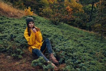 A young woman in a yellow raincoat enjoying nature on a serene hill in the forest during a peaceful travel break