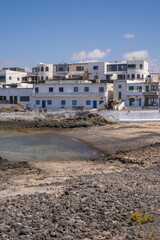 Fototapeta premium Bay and typical houses of the fishing village of Caleta de Caballo. White houses. Rock coast in the foreground. Turquoise water. Calm sea. Caleta de Caballo, Lanzarote, Canary Islands, Spain.