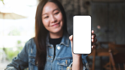 Mockup image of a young woman holding and showing a mobile phone with blank white screen