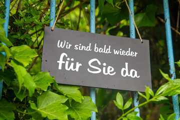 Symbolbild Betriebsferien: Schild am Garten mit der Aufschrift WIR SIND BALD WIEDER F&Uuml;R SIE DA