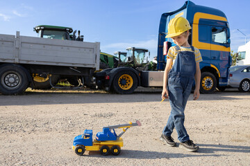 7-year-old boy plays with a toy car, and behind him are large cabins of commercial vehicles. interesting childhood of a child, games in the profession. The boy's interest in machines and their work. © Anna