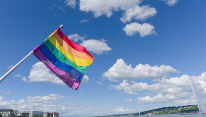 A six-band rainbow flag representing the LGBT community flutters in the wind on the Mont Blanc bridge and Lake Geneva