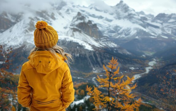 A person in a yellow jacket stands gazing at a majestic mountain in the background