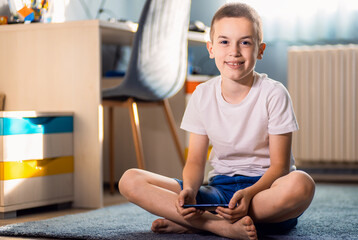Portrait of boy playing video game on smartphone sitting on floor in his room.
