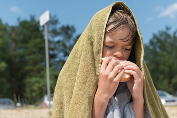 A little boy on the beach after swimming eats bread