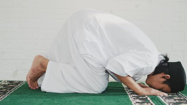 Side View Of Young Asian Muslim Man Praying To Allah And Taking Sujud Or Prostration Position At Mosque