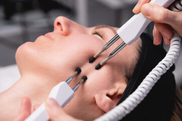 Close-up of a woman receiving an electric neck massage with equipment in a beauty salon. Used for...