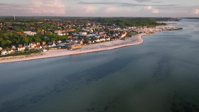 Aerial footage flying over Baltic Sea resort of Laboe, showcasing beach dotted with hooded beach chairs and marina. Camera tilts up and right, providing  panoramic view of resort Schleswig-Holstein.