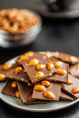 Broken chocolate bar with almonds on plate on black table.