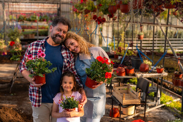 A smiling family holds potted flowers in a greenhouse, showcasing their shared love for...