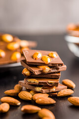 Broken chocolate bar with almonds on black table.
