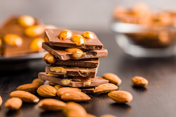 Broken chocolate bar with almonds on black table.