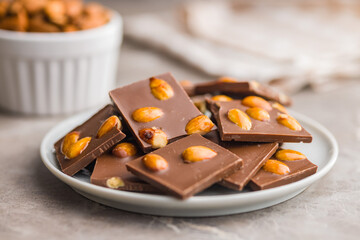 Broken chocolate bar with almonds on plate on kitchen table.