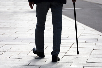 Silhouette of man walking with a cane down the street. Concept of old age, diseases of the spine or...