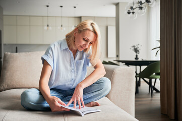 Woman sitting comfortably on couch, deeply engaged in reading book. Cozy living space with modern...