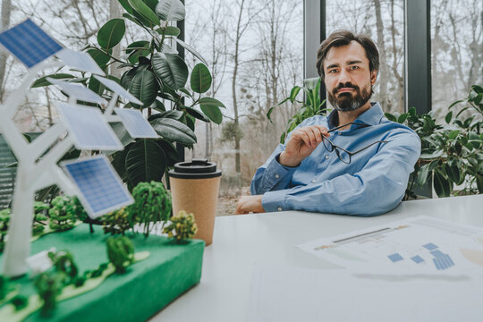 Businessman holding eyeglasses and sitting with solar tree project at desk