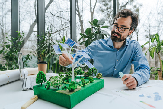 Smiling businessman working on solar panels model near laptop at desk