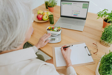 Nutritionist preparing diet plan sitting at table in home