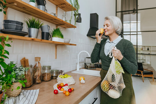 Woman smelling fruit standing in kitchen at home
