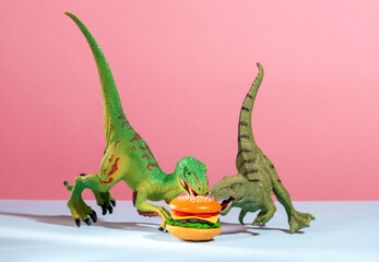 Obraz premium Two cute dinosaurs are fighting over burger. Humor and fast food concept.