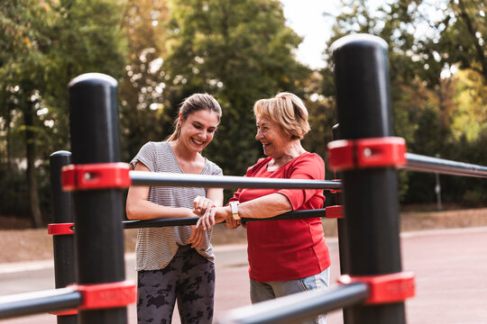 Happy young woman examining fitness tracker with grandmother in park