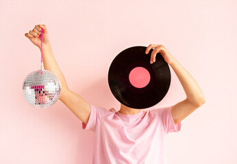 Portrait of man in pink shirt holding vinyl record near his face on pink background.