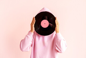 Portrait of man in pink hoodie holding vinyl record near his face on pink background.