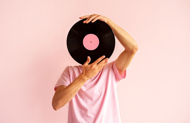 Portrait of man in pink shirt holding vinyl record near his face on pink background.