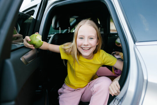 Happy girl holding apple and disembarking from car