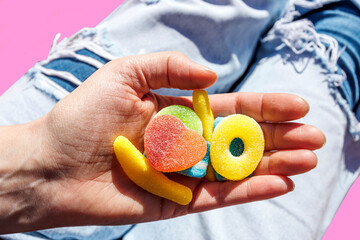 Hand of woman holding jelly candies over torn jeans