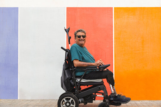 Happy senior man with disability in motorized wheelchair by colorful wall
