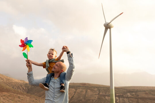 Father carrying son on shoulder with wind turbine in background