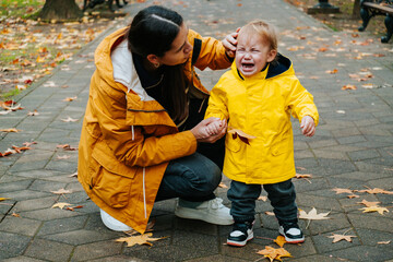 Young mother tries to calm her crying little son outdoor in the park. Raising  child concept.