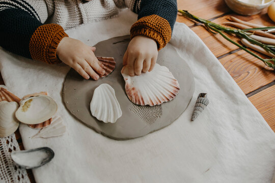 Boy making seashell imprint on clay at home