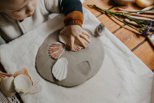 Boy making imprint of shells on clay at home
