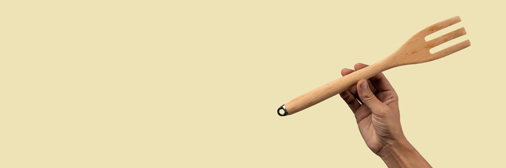 Hand holding wooden fork on beige background banner 