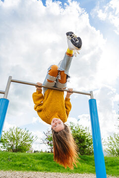 Happy girl hanging upside down on gymnastics bar at playground