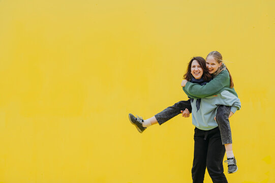Happy woman giving piggyback ride to daughter against yellow background
