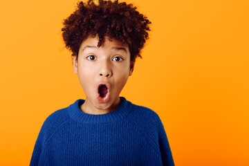 Young african american boy wearing bright colors expresses astonishment with wideopen mouth against a vivid orange backdrop