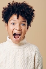 Joyful expression of a young african american boy with mouth open and eyes wide in surprise on beige background